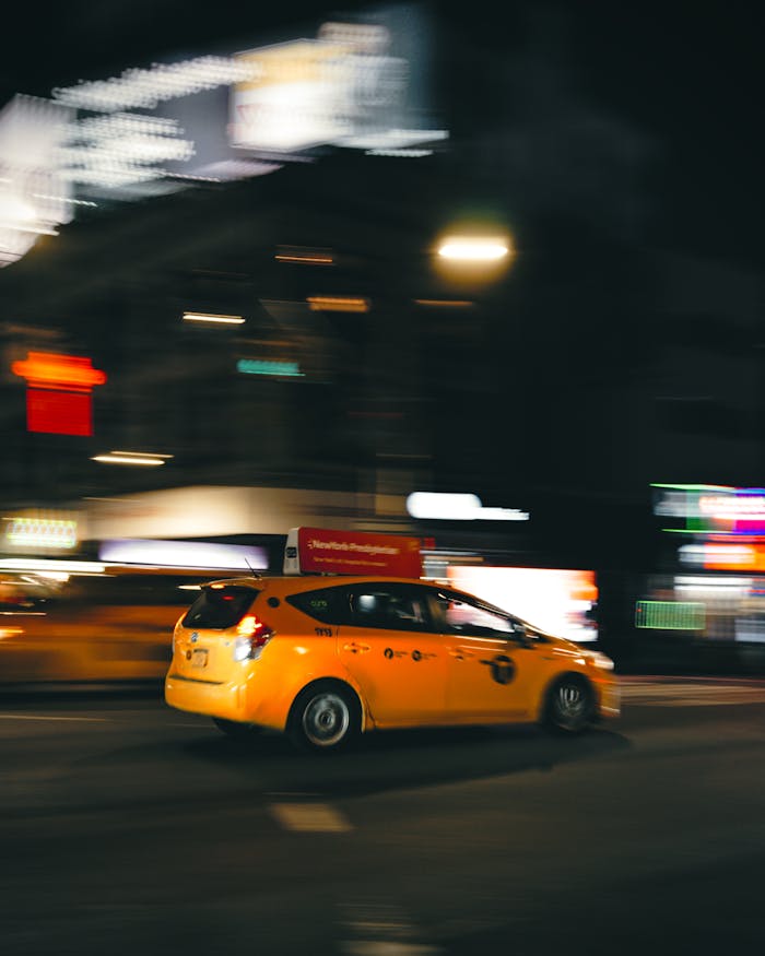 Blurred motion of a speeding yellow taxi on a New York City street at night.