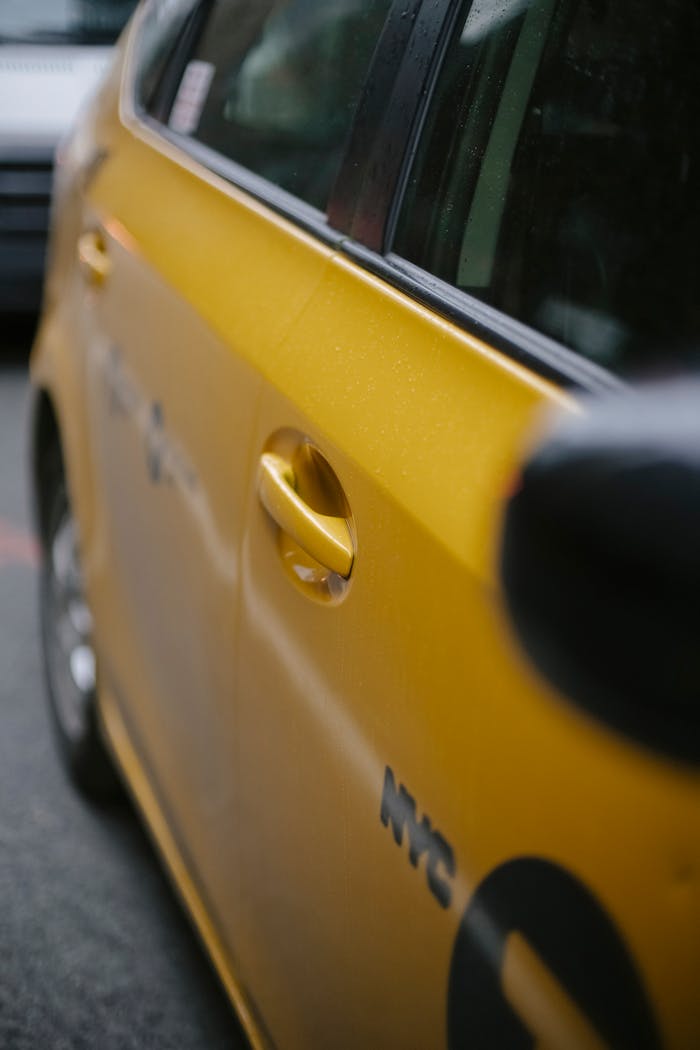 A detailed view of a yellow NYC taxi door in an urban street setting.